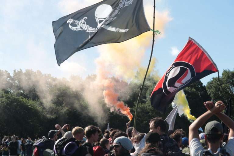 Avant de s'élancer hors du camp le samedi matin, les activistes en ont fait le tour, en formation, à grands renforts de chants et fumigènes. Les drapeaux anarchistes, écologistes et antifascistes ont flotté au-dessus du camp comme dans les cortèges toute la durée des événements. Photo Pierre-Olivier Chaput pour Radio Parleur.