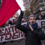 Manifestation 5 décembre grève générale, une femme brandit un drapeau rouge, symbole de la Commune de Paris