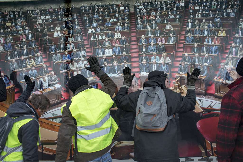 Le 8 février 2018, des Gilets Jaunes manifestent devant l'Assemblée Nationale à Paris. Frappant sur les panneaux de bois qui la protège, ils tentent d'interpeller leurs député.es et réclament une démocratie plus directe. Photo : Sylvain Lefeuvre pour Radio Parleur